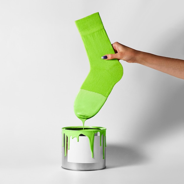 A woman's hand dips her green sock into a can of paint