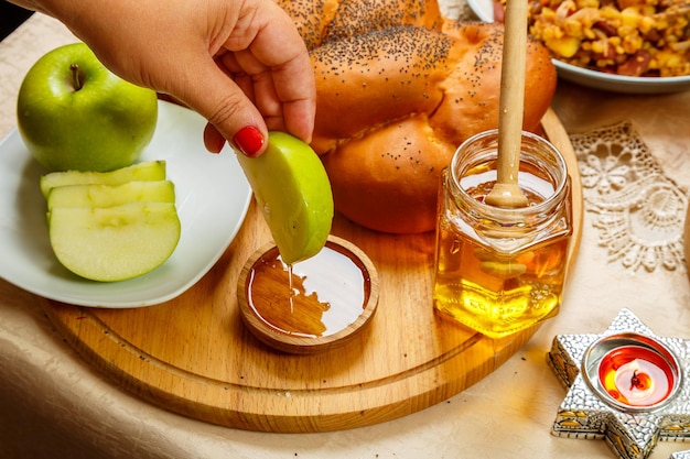 A woman's hand dips a piece of apple in honey at the table in honor of the celebration of Rosh Hashanah