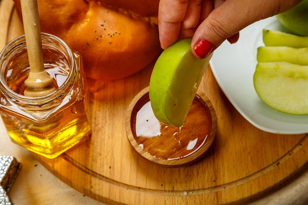 A woman's hand dips a piece of apple in honey at the table in honor of the celebration of Rosh Hashanah