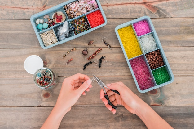 Photo woman's hand fixing the hook on beads with plier on wooden desk