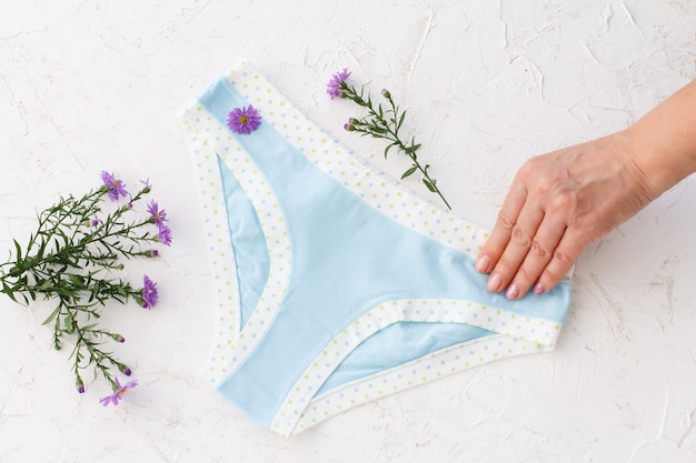 woman's hand holding beautiful blue cotton panties with flowers around on white background