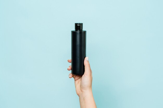 Woman's hand holding black bottle of cosmetic product for shower on blue background