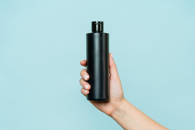 Woman's hand holding black bottle of cosmetic product for shower on blue background