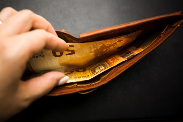 Woman's hand holding a black wallet with euro money.