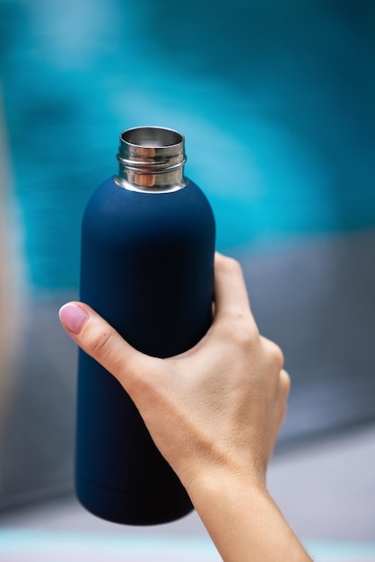 A woman's hand holding a blue stainless steel water bottle.