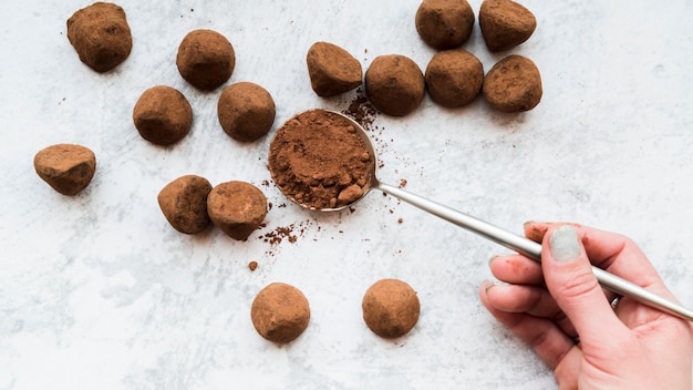 Photo a woman's hand holding cocoa powder in spoon on white textured backdrop