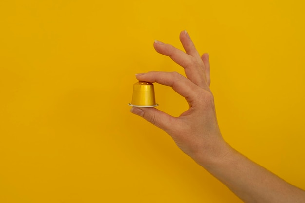 Woman's hand holding a coffee capsule on a yellow background