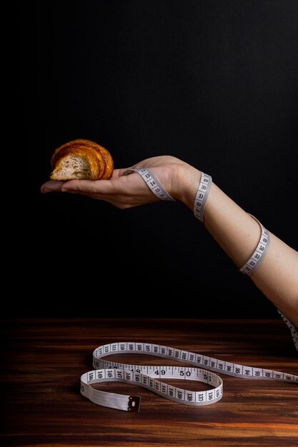 Photo woman's hand holding croissant with measuring tape wrapped around her arm, strict diet concept