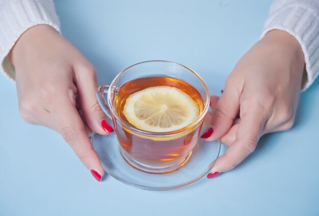 Woman's hand holding cup of tea with piece of lemon