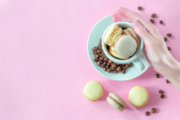 La mano della donna che tiene la tazza piena di cioccolato dolce macarons al limone sul piatto con i chicchi di caffè su sfondo rosa pasticceria dolci dolci gustosi zucchero foodcopy spazio