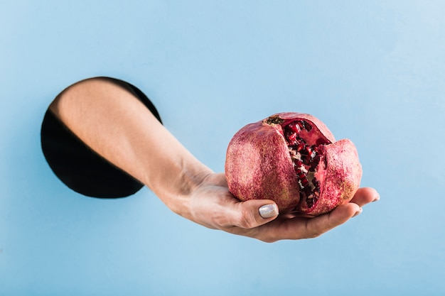 woman's hand holding a cut grenade out of a black hole in a blue paper wall.