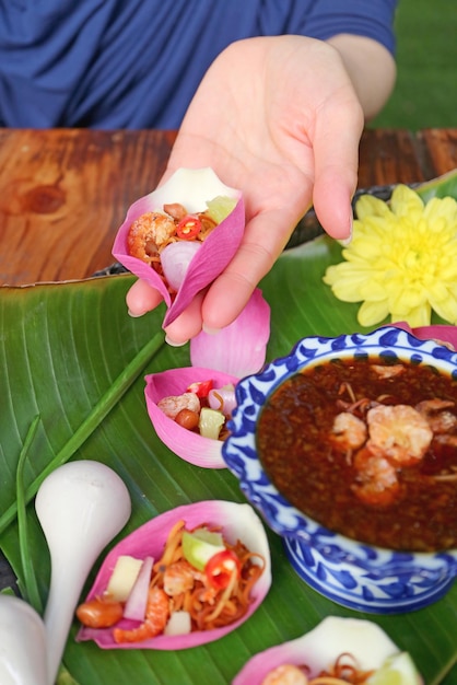 スパイシーなディップを入れる前に、新鮮な蓮の花びらを包んだ前菜を持つ女性の手