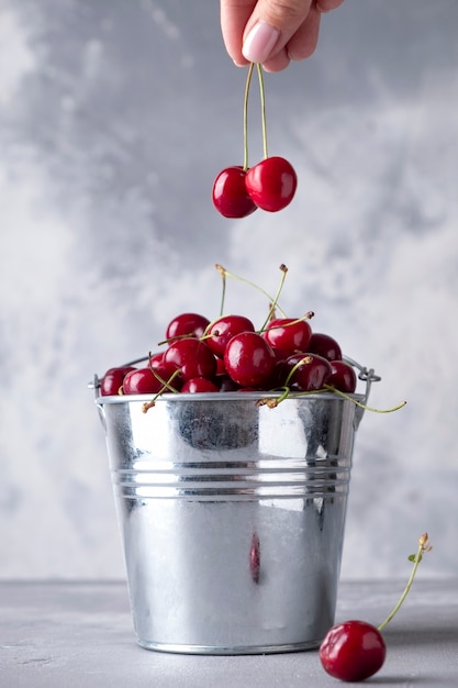 Woman's hand holding fresh sweet cherry under full metal bucket with cherry.