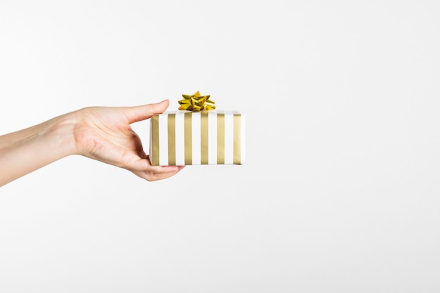 Woman's hand holding a gift in white and gold paper on gray.