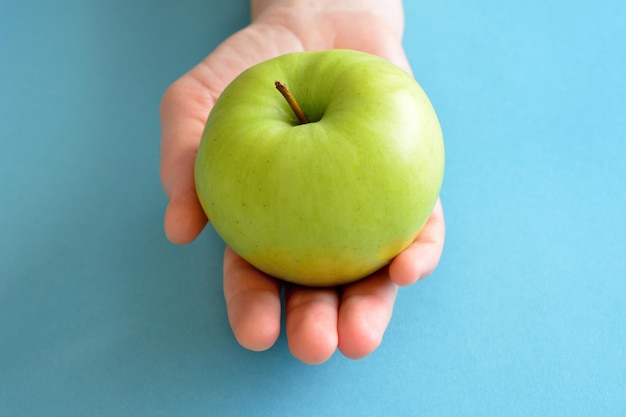 woman's hand holding green apple on the blue background