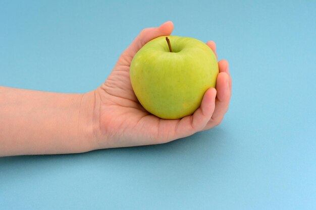 woman's hand holding green apple on the blue background