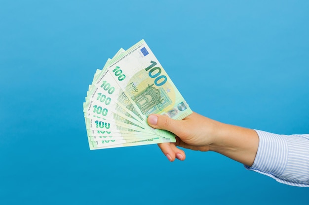 Woman's hand holding hundred euros banknotes isolated on blue background Euro money cash banknotes