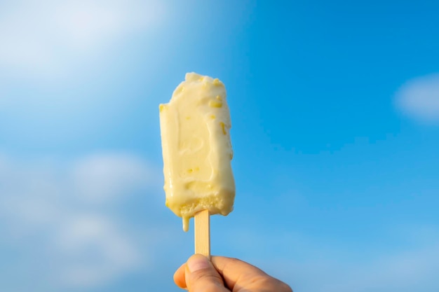 A woman's hand holding ice cream raised to the sky In summer
