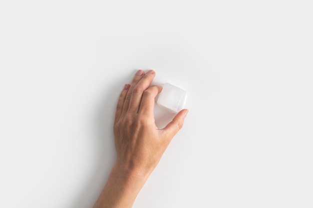 Woman's hand holding an ice cube on a white background Top view flat lay