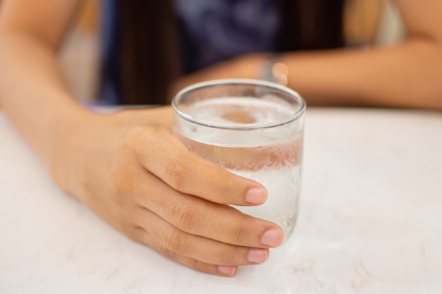 Woman's hand holding ice water in glass with blur background.