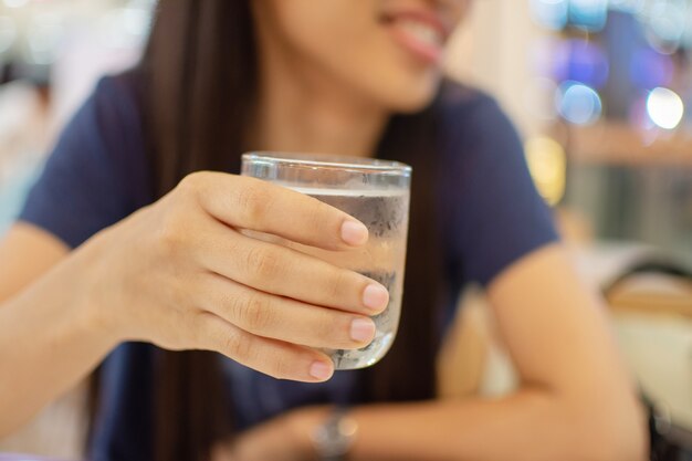 Woman's hand holding ice water in glass with blur background. 