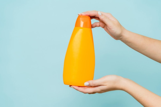 Woman's hand holding packaging of shampoo or conditioner on a blue background Copy space and mock up