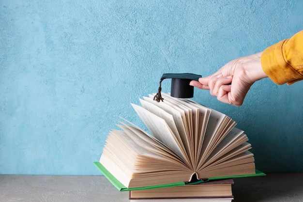 Woman's hand holding a paper student hat over an open book