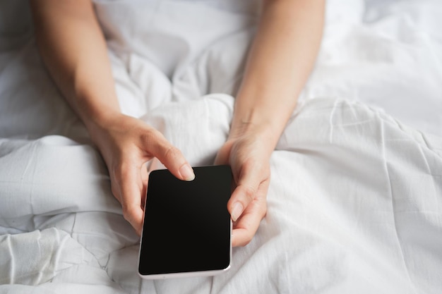 Woman's hand holding phone with black blank screen on bed Clipping path