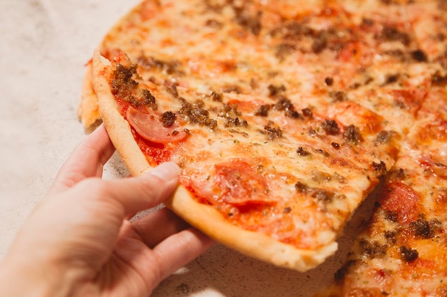 Woman's hand holding a piece of pizza. Time to eat, order at home.