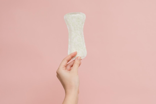 Woman's hand holding sanitary pad on pink background