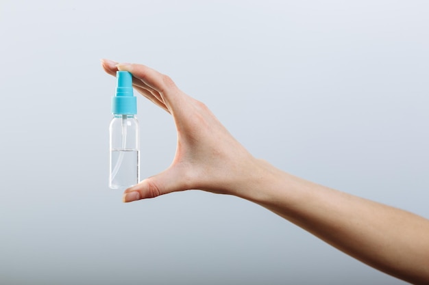 Woman's hand holding spray bottle sanitizer isolated on gray background