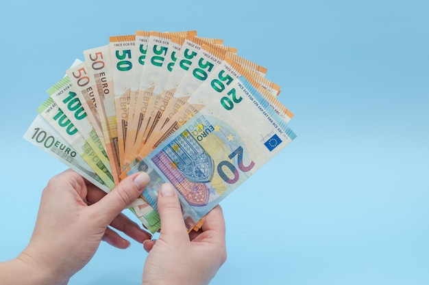 파란색 배경에 돈 유로의 스택을 들고 여자의 손