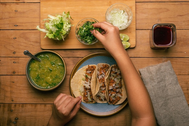 woman's hand holding a taco of marinated meat Plate with tacos sauce and vegetables on wooden table