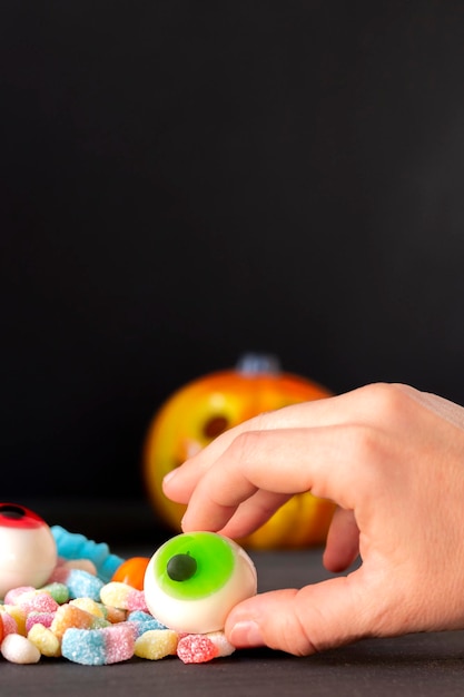 Woman's hand holding a terrifying candy eye during Halloween party along with many other delicious sweets, close up, selective focus