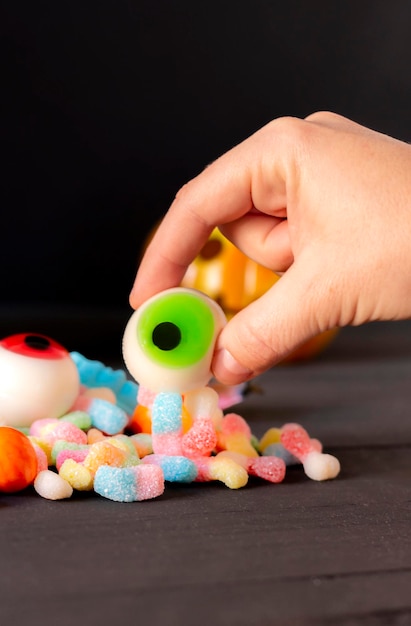 Woman's hand holding a terrifying candy eye during Halloween party along with many other delicious sweets, close up, selective focus