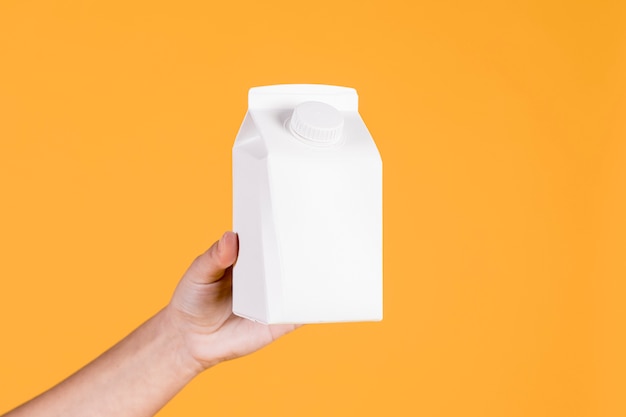 Woman's hand holding tetra pack in yellow background