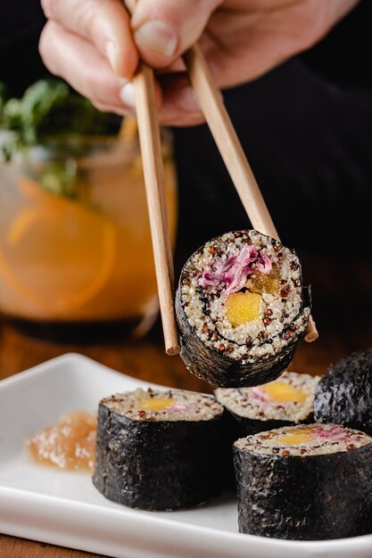 Woman's hand holding vegan sushi roll with wooden chopsticks