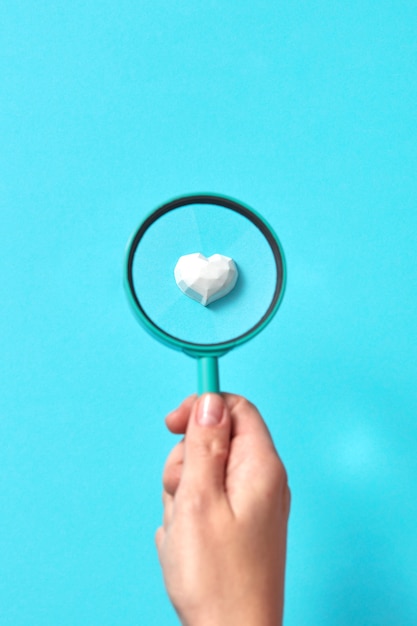 Woman's hand holds big magnifying glass above plaster figure of heart in set