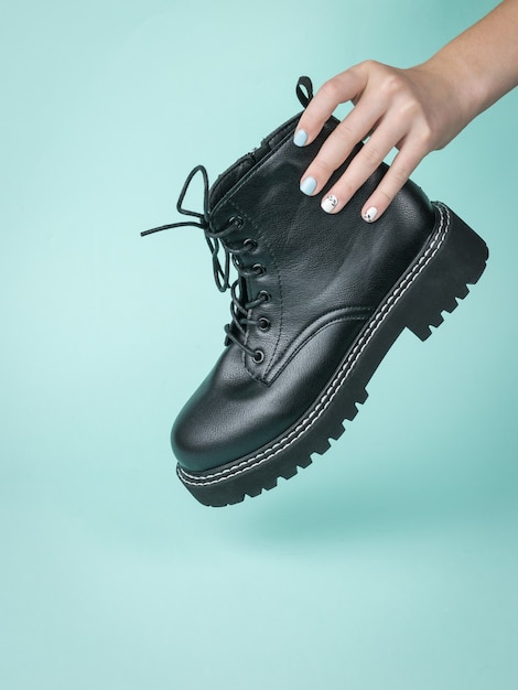 A woman's hand holds a brutal leather shoe on a blue surface