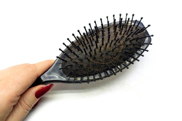 A woman's hand holds a comb with a lot of hair on it. Concept of Hair Loss, Alopecia, Baldness