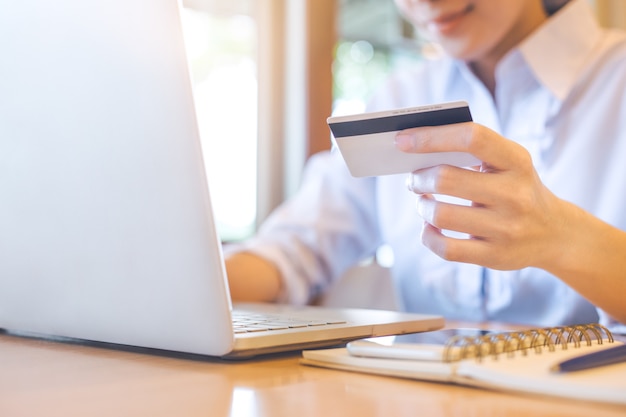 La mano di una donna tiene una carta di credito e usa un laptop per fare acquisti online