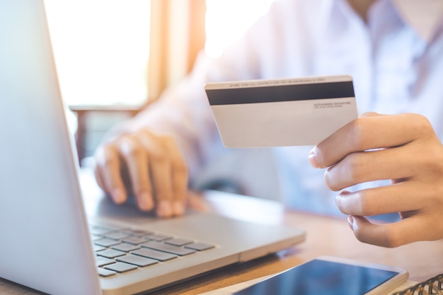 A woman's hand holds a credit card and uses a laptop to shop online.