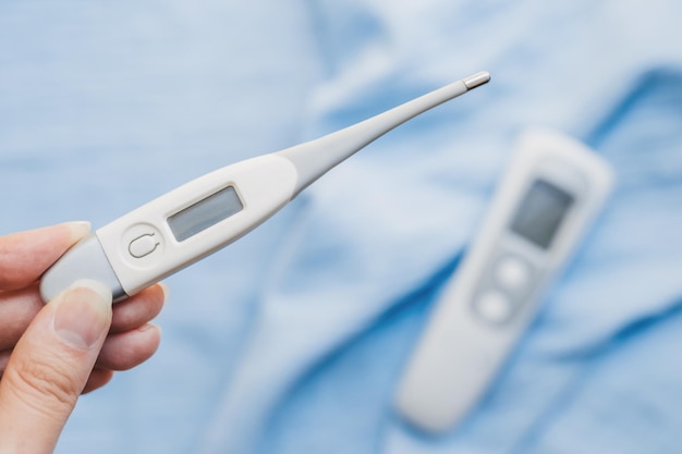 A woman\'s hand holds an electronic thermometer to measure body\
temperature on a blue background