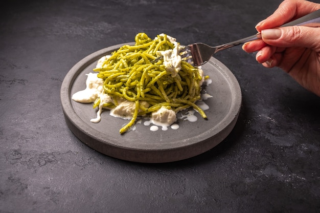 Woman's hand holds a fork with a paste with strachatella and pesto, selective focus, close up