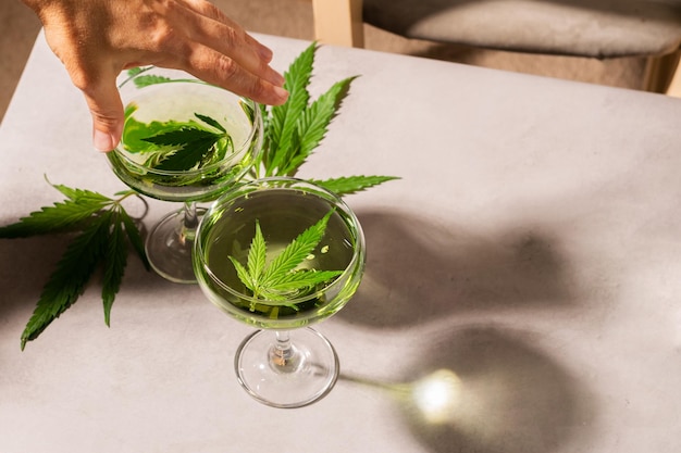 女性の手は、SBD 麻ライト コンクリート背景ハード シャドウから緑の飲み物でガラスを保持しています。