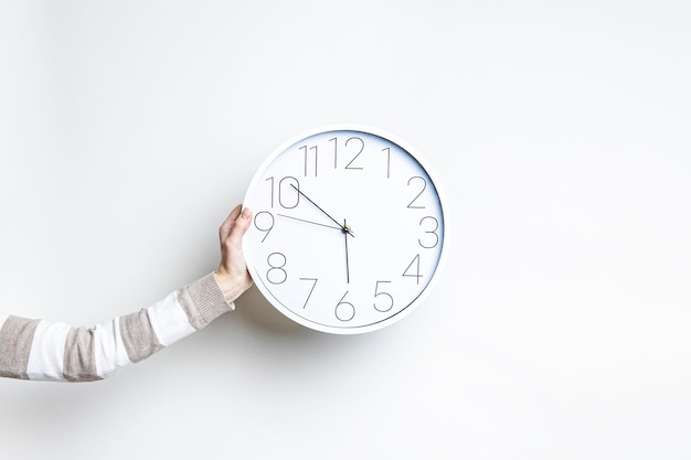 Photo woman's hand holds a large white clock against a light wall.