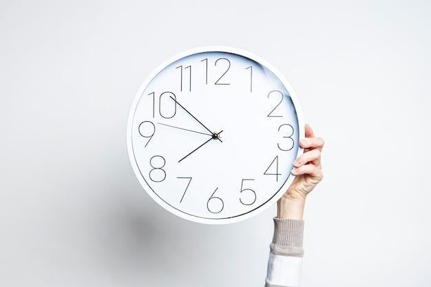 Woman's hand holds a large white clock on a light background.