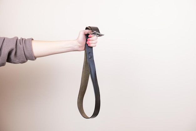 woman's hand holds a leather trouser belt with a metal buckle. the concept of physical punishment of children, a metaphor for abuse. space to insert text.