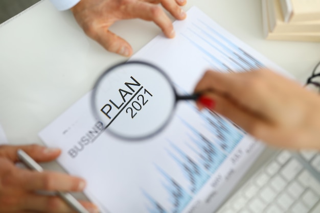 Woman's hand holds magnifying glass over business plan for 2021