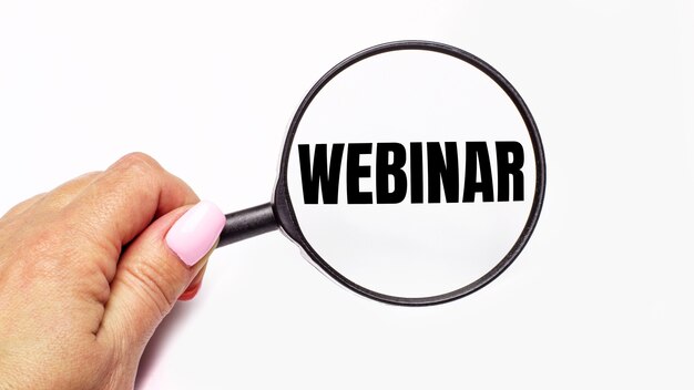 Woman's hand holds a magnifying glass with the inscription WEBINAR